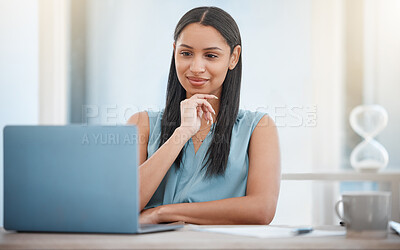 Young mixed race business woman holding hand on chin while working on laptop. One female entrepreneur smiling while reading an email or getting an idea while looking at laptop screen in her office