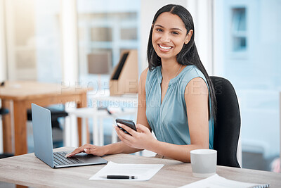 Confident young mixed race businesswoman texting on cellphone while working on laptop in an office. One female only checking browsing apps and online media on smartphone to manage her startup plans