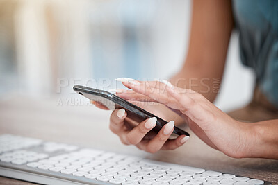 Closeup of hands of businesswoman scrolling online apps on her cellphone while sitting at her desk. Freelance entrepreneur working in front of her computer keyboard, texting on her smartphone