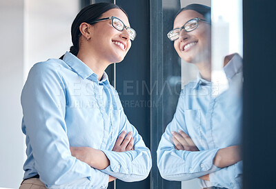 Confident empowered mixed race businesswoman wearing glasses and looking out a window with arms crossed in an office. One female only thinking and dreaming about goals, vision and success for startup