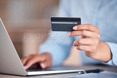 Unrecognizable businessperson holding a credit card in their hand while working on a laptop at a desk at work. One unrecognizable shopping online using their laptop and paying with a card at work