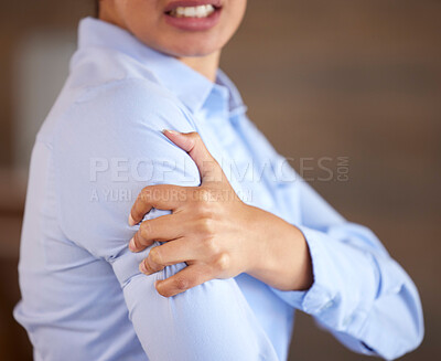 Closeup of unknown mixed race businesswoman standing alone and suffering from sore shoulder or arm while working in an office. Hispanic professional in pain while holding an injury. Injured on the job