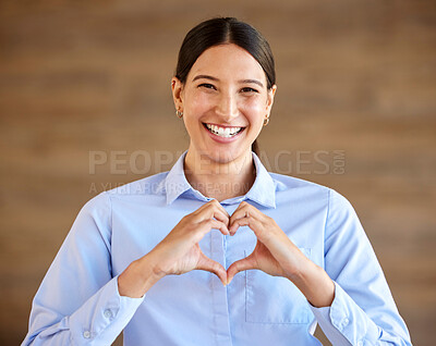 Young happy hispanic businesswoman smiling and standing and making a heart gesture with her hands alone at work. Cheerful and positive mixed race female making a heart with her hands in an office