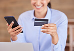 Unrecognizable mixed race businesswoman smiling while using a phone and credit card sitting alone in an office at work. Happy hispanic female shopping online and paying with her card