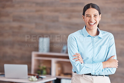 Young happy cheerful mixed race businesswoman smiling while standing with her arms crossed alone in an office at work. One hispanic female boss standing while working at a startup company