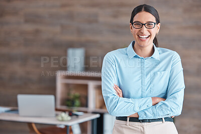 Portrait of a young happy cheerful mixed race businesswoman wearing her spectacles smiling while standing with her arms crossed alone in an office at work. One hispanic female boss standing while working at a startup company