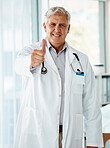 Happy mature caucasian male doctor smiling while showing a thumbs up working at a hospital alone. One senior man wearing a labcoat standing and expressing support with a hand gesture at a clinic