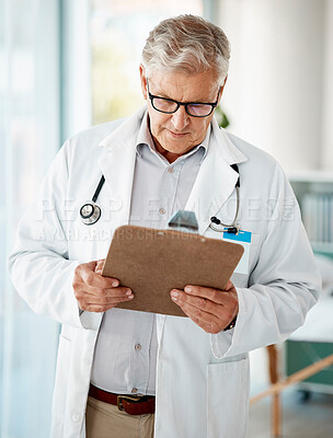 Buy stock photo Handsome mature male caucasian doctor in white lab coat looking out at paperwork on a clipboard. One senior man holding medical or patient records while looking trying to diagnose a condition