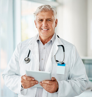 Buy stock photo Mature caucasian male expert doctor smiling while using a digital tablet working at a hospital alone. One senior man wearing a labcoat and working on a digital tablet standing in an office at a clinic