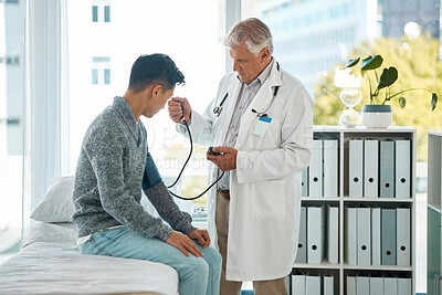 Buy stock photo Mature caucasian male doctor doing a checkup checking a young patient's blood pressure at a hospital. Young asian man sitting on a bed doing routine health tests with a gp. Healthcare is important