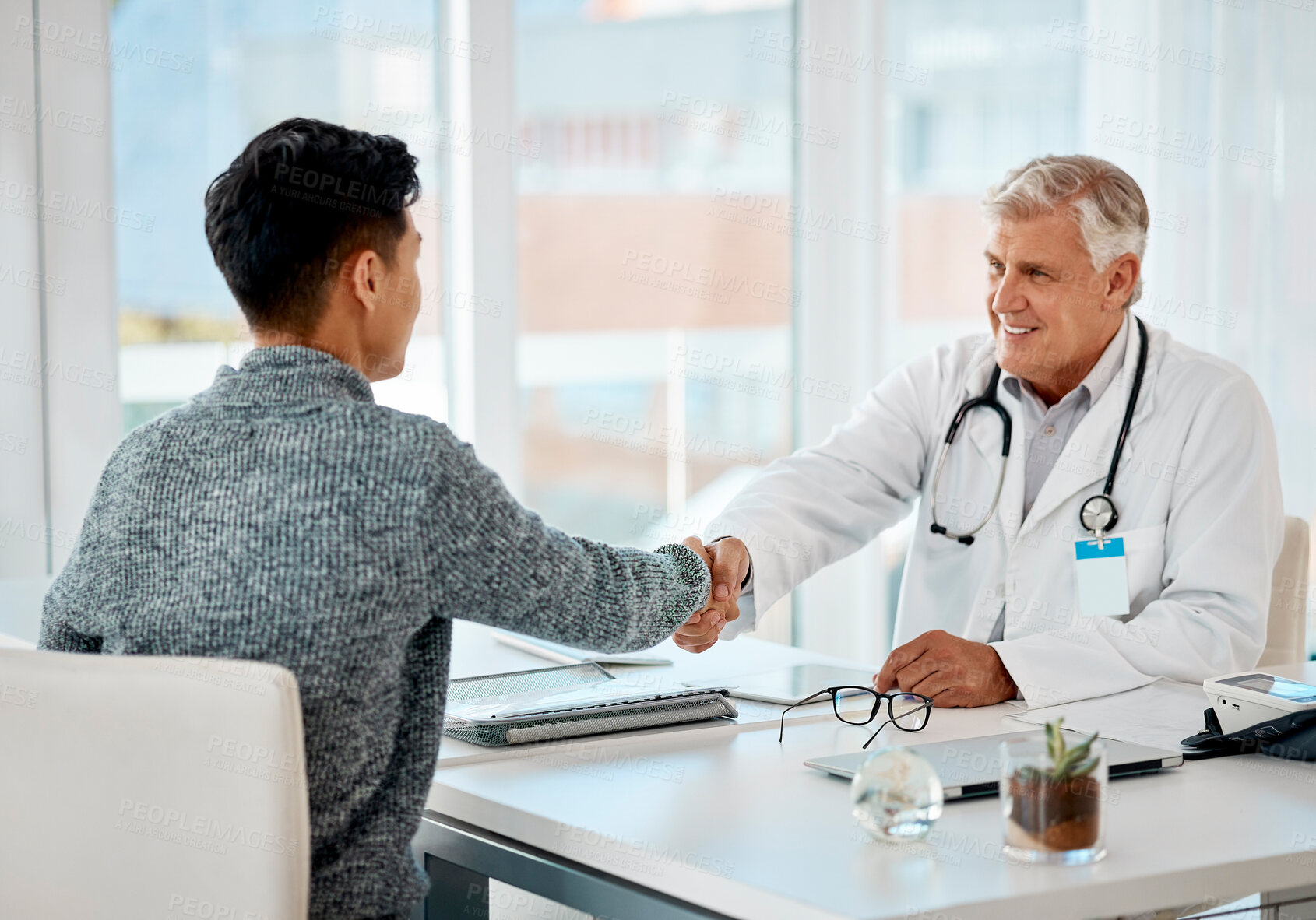 Buy stock photo Mature caucasian doctor greeting a patient with a handshake for a consultation. Senior medical professional smiling in meeting with a patient at the hospital. Two men greeting during a consult