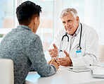Mature caucasian medical doctor sitting with his patient during a consultation in a clinic and talking. Healthcare professional using hand gestures while discussing treatment with sick mixed race man