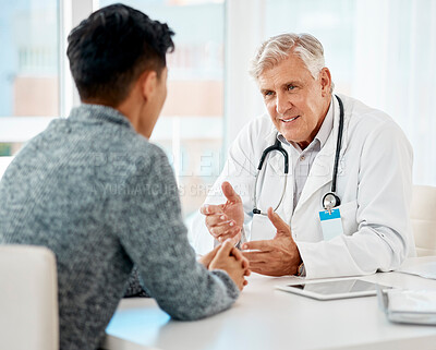 Buy stock photo Mature caucasian medical doctor sitting with his patient during a consultation in a clinic and talking. Healthcare professional using hand gestures while discussing treatment with sick mixed race man