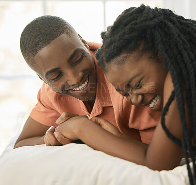 Buy stock photo Affectionate young african american couple holding hands while relaxing together on a bed at home. Happy black boyfriend and girlfriend sharing intimate moments in a loving relationship while bonding