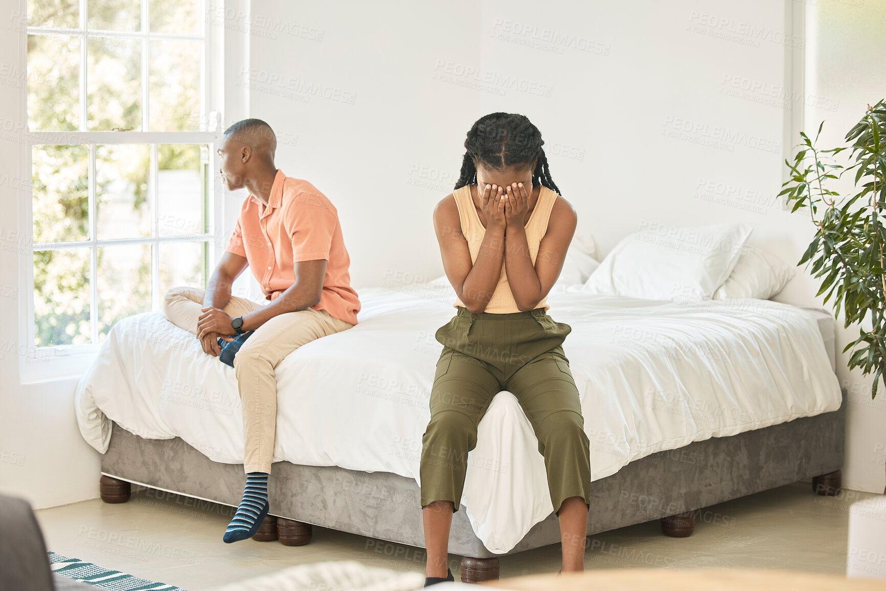 Buy stock photo Unhappy young african american couple in a bedroom sitting separate on a bed during an argument. Young black woman in her 20s covering her face looking sad while fighting with her boyfriend at home