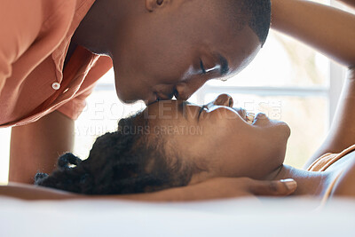 Buy stock photo Young happy african american couple bonding and enjoying time together lying on a bed together at home. Boyfriend kissing his girlfriend on the forehead while relaxing together on the weekend

