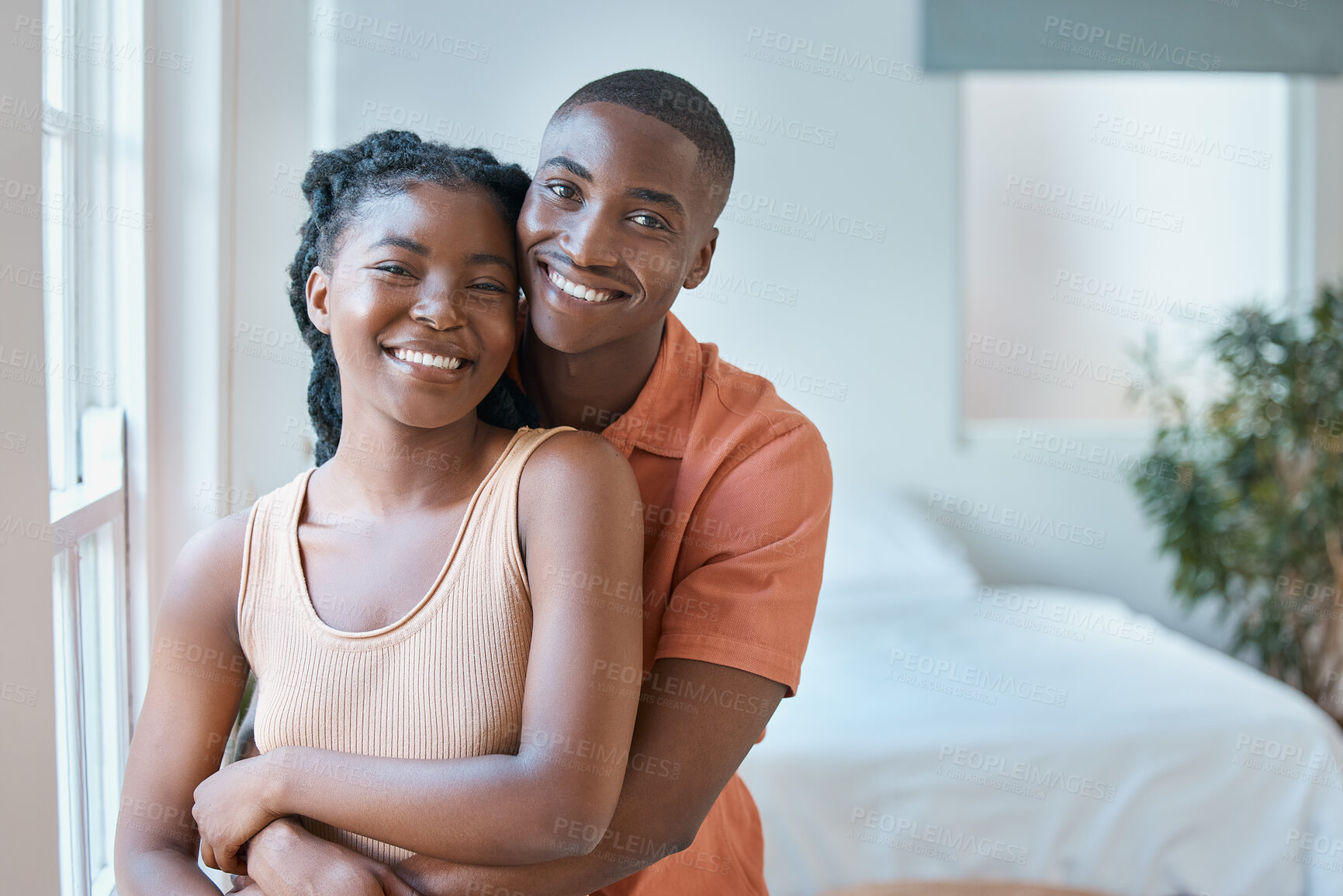 Buy stock photo Portrait of a young black african american couple smiling as they lovingly embrace in the bedroom at home. An affectionate good looking black man and woman spending time together and looking in love