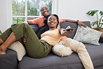 Young african american couple changing channels on remote and watching television together on sofa at home. Girlfriend relaxing on boyfriend's lap while enjoying entertainment shows, series and movies