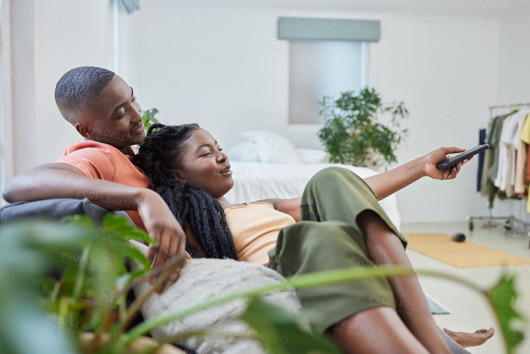 Buy stock photo Young african american couple changing channels on remote and watching television together on sofa at home. Girlfriend relaxing on boyfriend's lap while enjoying entertainment shows, series and movies