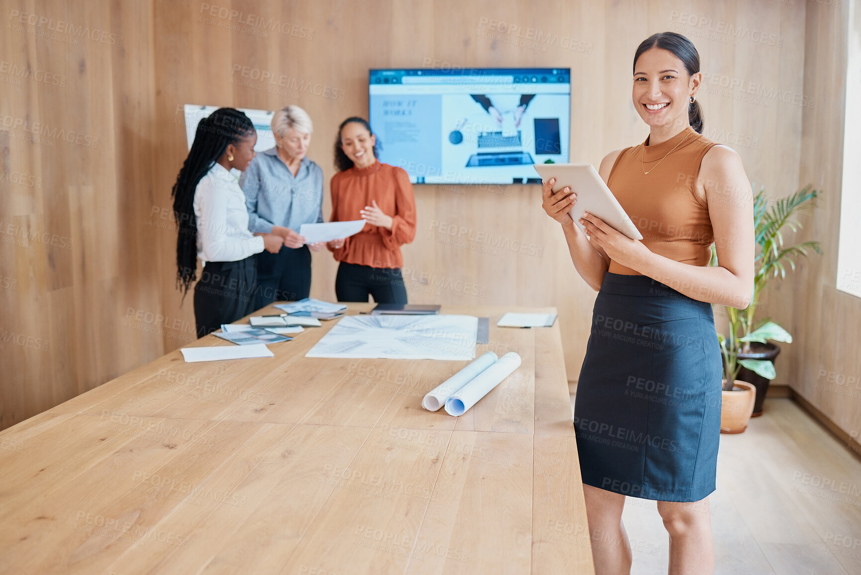 Buy stock photo Young happy mixed race businesswoman holding and working on a digital tablet while standing in a meeting at work. One hispanic female boss smiling while using a digital tablet in a boardroom