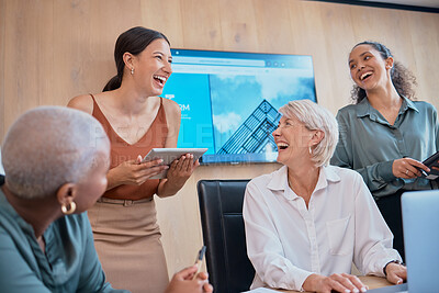 Four happy businesswomen laughing and working together in a boardroom at work. Young cheerful mixed race woman using a digital tablet while doing a presentation in a meeting with coworkers