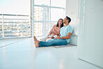 Full length of young happy mixed race couple sitting together on floor of their new apartment and drinking coffee. Smiling hispanic couple bonding and laughing while enjoying the morning as homeowners