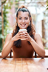 Happy young mixed race woman enjoying a cup of coffee on a break at a cafe in the city. One female only drinking a warm beverage in a disposable takeaway paper cup while relaxing outside a restaurant
