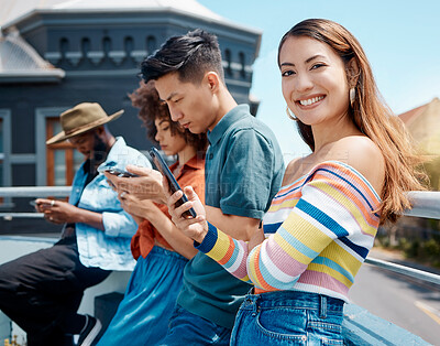 Buy stock photo Portrait of beautiful young smiling asian woman standing outside with friends and using her cellphone to browse the internet. Group of diverse millennials using their phones to connect to social media