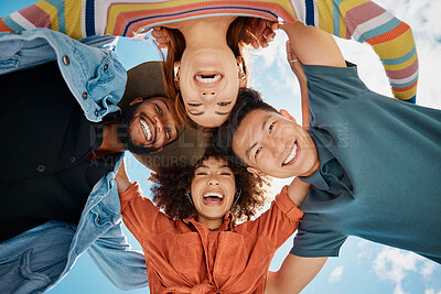 Buy stock photo Group of diverse friends standing in a huddle against a blue sky. Multi-racial friends standing together arms around each other and smiling while looking down at the camera 