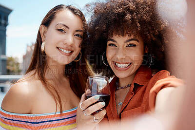 Buy stock photo Two beautiful mix race women smiling taking a selfie while enjoying a glass of red wine while outdoors at a party. Hispanic female with cool afro hairstyle enjoying her time with a friend on a sunny day while enjoying a beverage 
