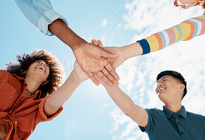 Buy stock photo A low close up view of a group of diverse young friends joining hands in a huddle while smiling with a blue sky in the background on a sunny day. Mixed race female with a cool afro hairstyle and her asian man friend showing unity with a group of friends