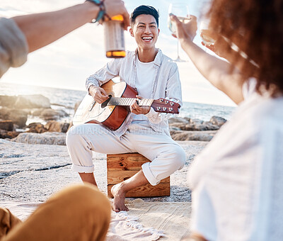 Buy stock photo Close up of a young asian male playing the guitar for his friends outside on the beach while having alcohol