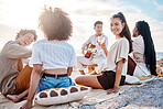 A young man at the beach playing his guitar with his two female friends. Diverse group of friends listening music on a sunny day