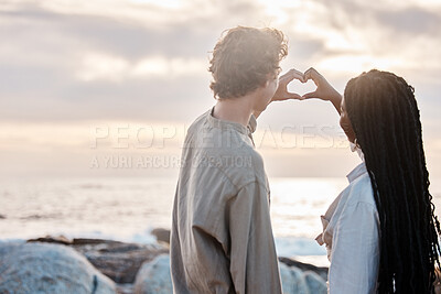 Buy stock photo Rear view of a young multiracial couple being romantic by making a heart gesture with their hands at the beach