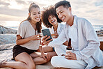 Three friends relaxing and using a phone while sitting and having alcohol at the beach