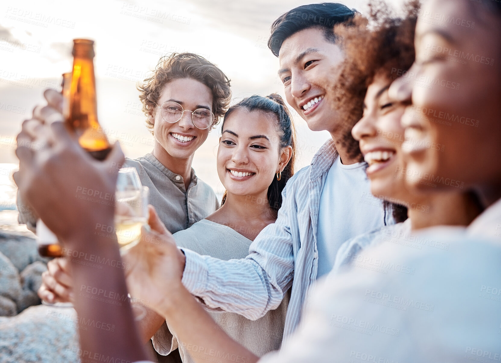 Buy stock photo Friends, group and cheers with alcohol on beach for celebration, bonding and holiday reunion or diversity in Bali. People, drinks and toast to summer break, fun adventure and relax on rocks at ocean