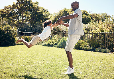 Cheerful african american dad swinging his son by the arms. Father playing with his son while spending time together outdoors at the park or in their backyard on a sunny day