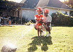 Father playing with his son outside. Little boy dressed as firemen. African American boy playing outside on a sunny day. Young male playing with a hosepipe in the garden. Dad and son spraying water from a hosepipe.