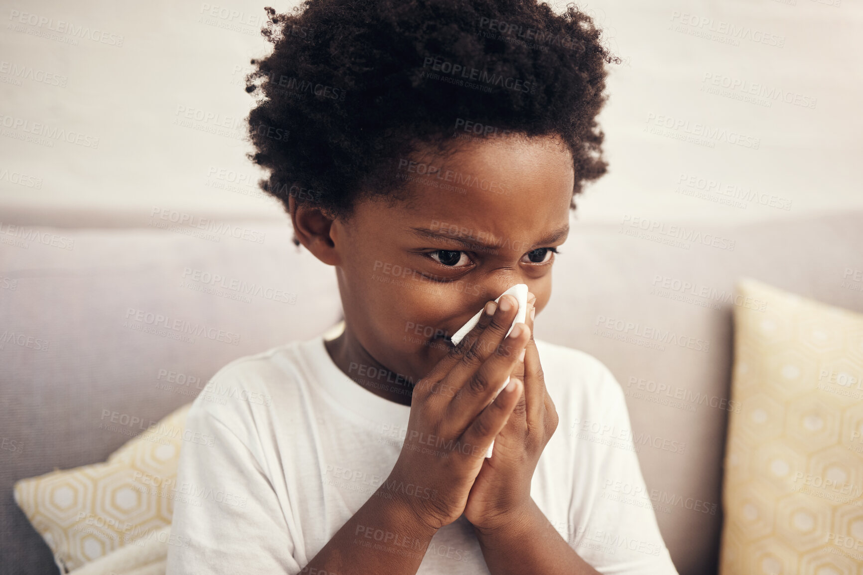 Buy stock photo Cold and flu season. Sick african american boy with afro blowing nose into tissue. Child suffering from a runny nose or sneezing, covering his nose while sitting at home. Time to get vaccinated 