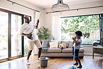 Mature african american dad and his young little son pretending to play the guitar by using a broom in a lounge at home. Black man and his boy having fun while cleaning their home together