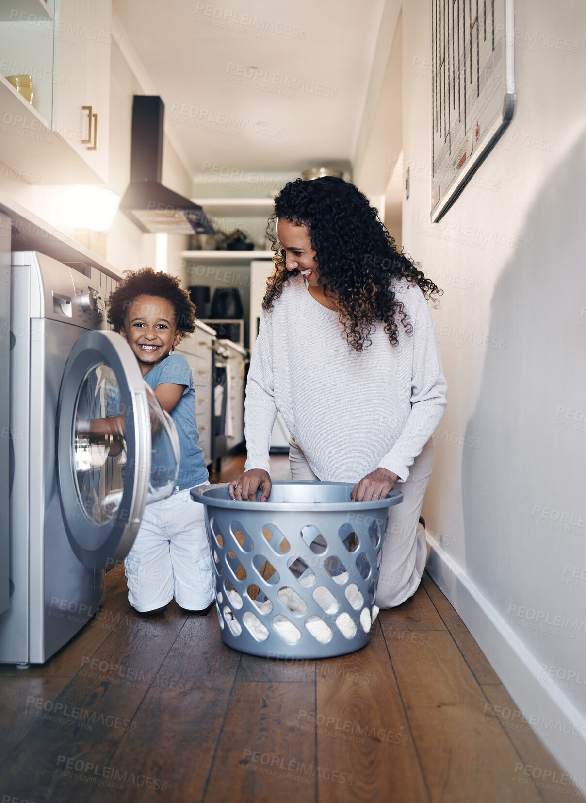 Buy stock photo Adorable little African American boy with an afro smiling and faving fun while doing housework with him mother at home. mixed race portrait of a cute child folding laundry with his mom