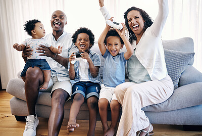 Buy stock photo Happy young african american family sitting on a sofa in the living room at home and celebrating a win. Adorable mixed race boys playing video games with consoles while their parents cheer for them