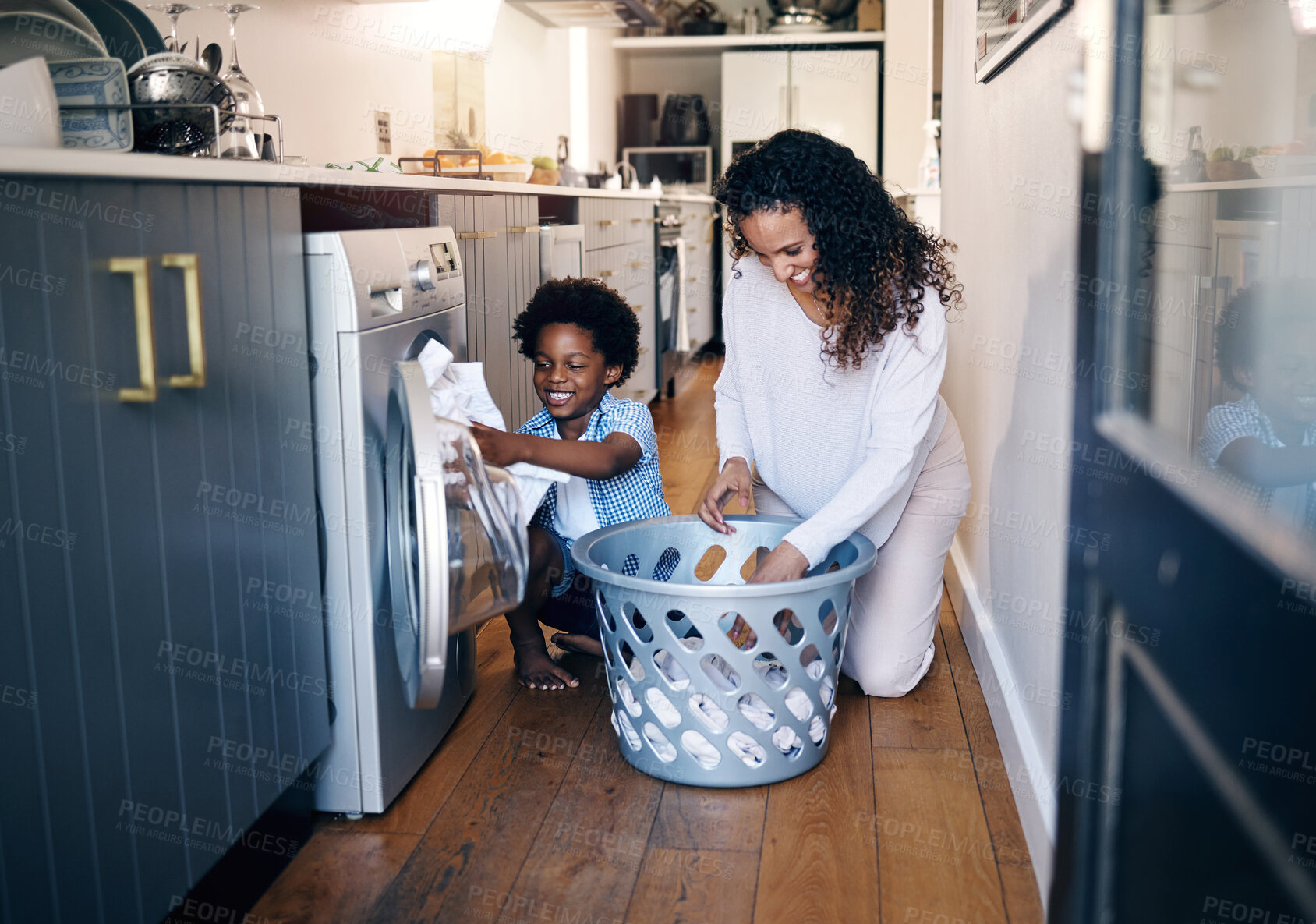 Buy stock photo Adorable little African American boy with an afro smiling and faving fun while doing housework with him mother at home. mixed race shot of a cute child folding laundry with his mom 