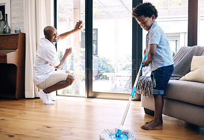 Buy stock photo Mature african american dad and his young little son doing housework in the lounge at home. Black man and his boy having fun while cleaning their home together. Black boy and his dad cleaning 