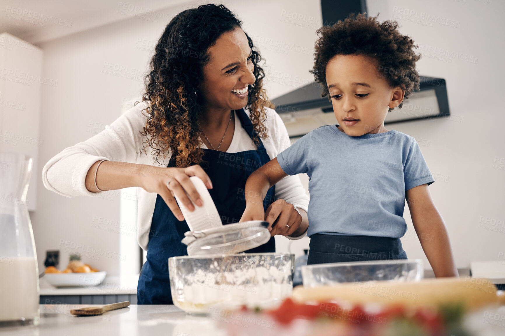 Buy stock photo Adorable little boy with afro baking in the kitchen at home with his mom. Cheerful mixed race woman sifting flour and mixing ingredients with the help of her son. Baking is a bonding activity