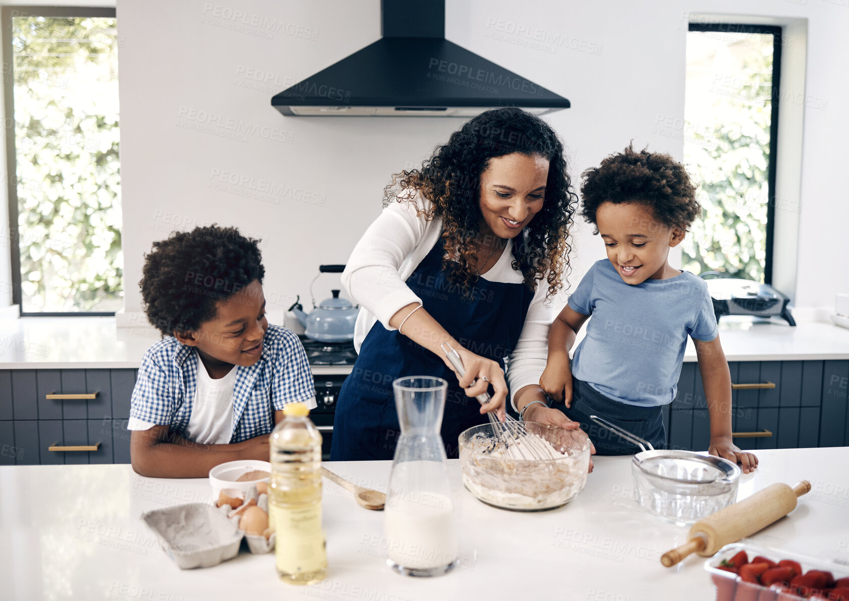 Buy stock photo Adorable little boy with afro baking in the kitchen at home with his mom and brother. Cheerful mixed race woman mixing ingredients with the help of her little boys. Baking is a bonding activity