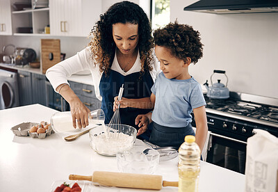 Mixed race woman standing and teaching her adorable little son how to bake in a kitchen at home. Cute hispanic boy helping his mother cook. African American parent bonding with her child on a weekend