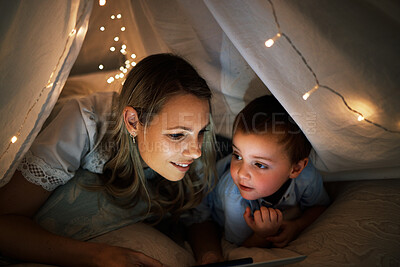 Shot of a beautiful young cheerful caucasian woman lying under a blanket fort with her adorable little son. Young family of two streaming movies on the internet while having fun and smiling together at home with wireless tablet