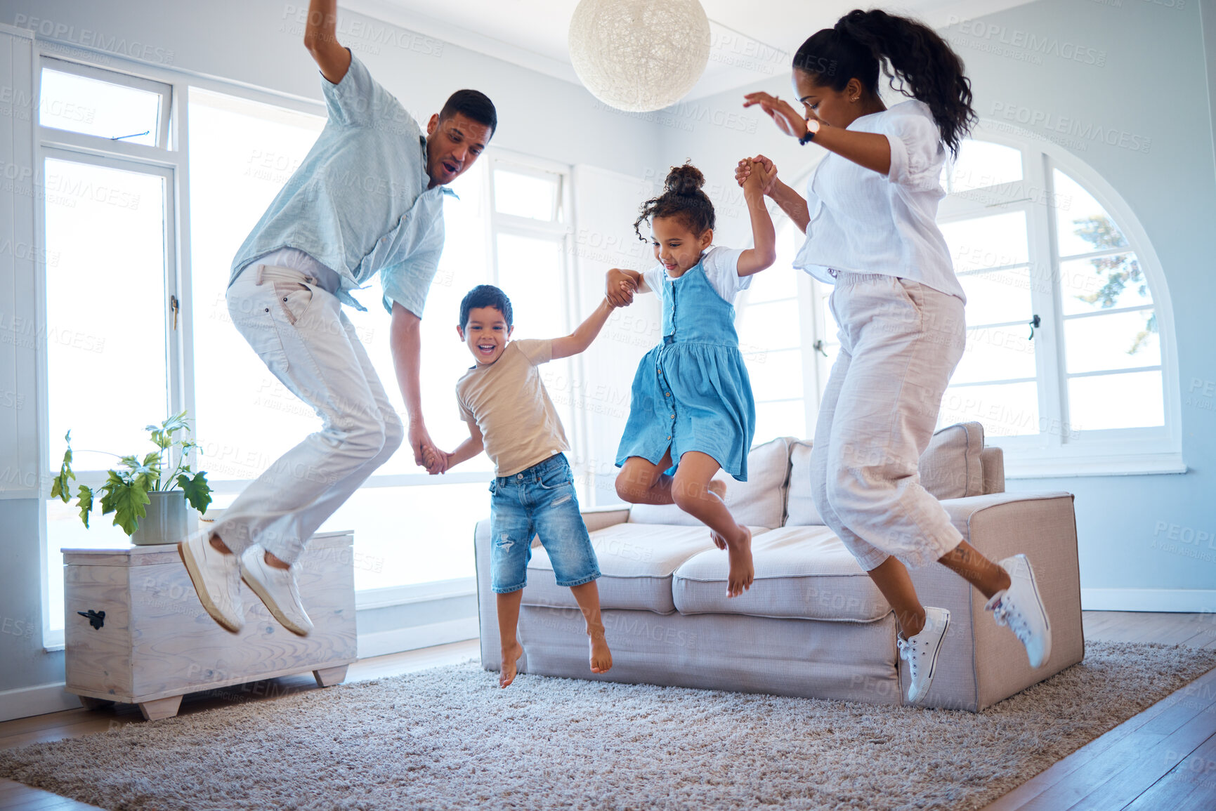 Buy stock photo Young parents jumping and playing with their two children at home. Happy hispanic family having fun spending time together. Little boy and girl holding hands and jumping in the air with mom and dad