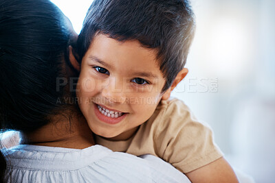 Buy stock photo Closeup portrait of adorable little boy smiling while lying on his mother's shoulder. Mixed race mother showing her son love and affection while spending time together at home 